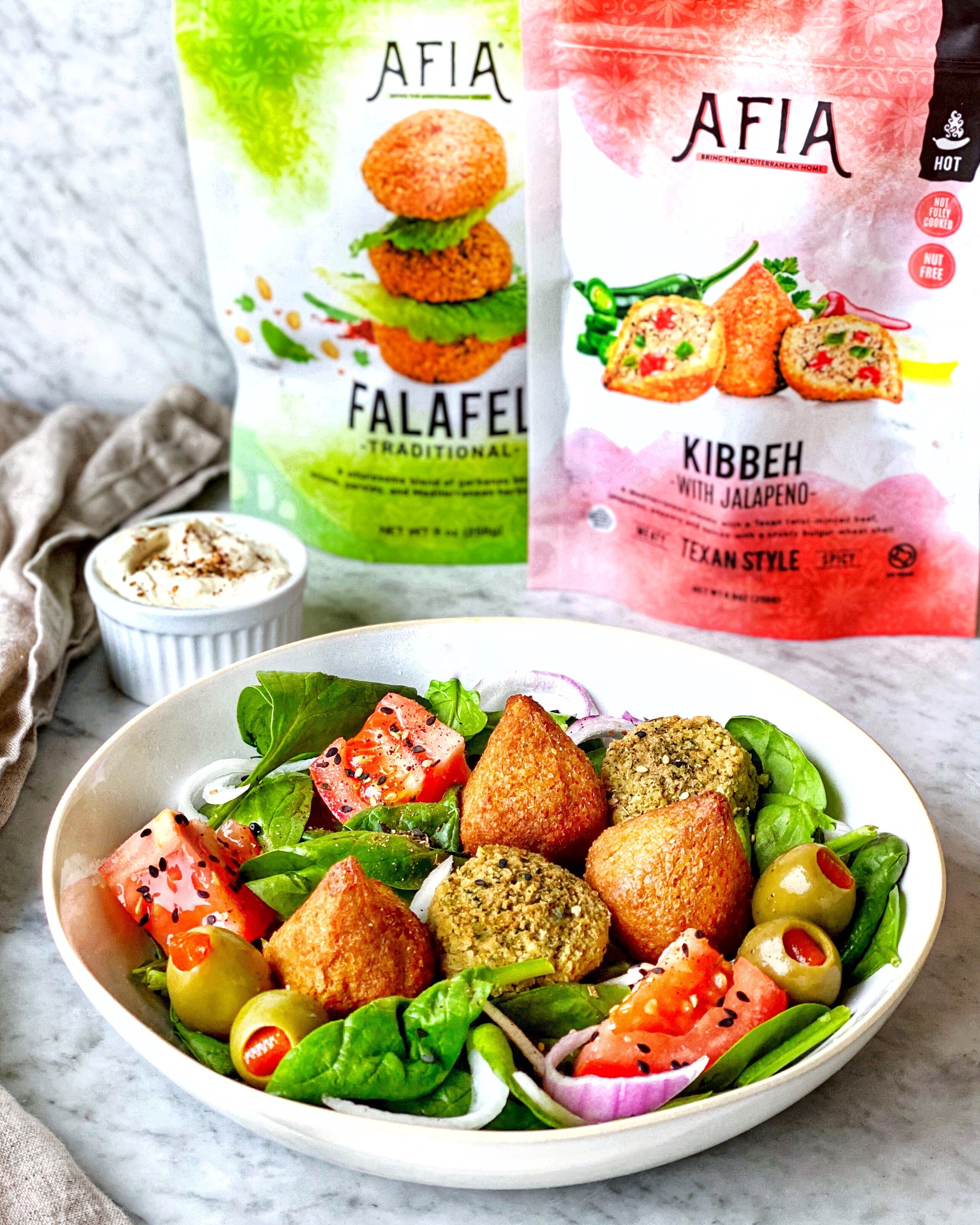 Spinach salad in a bowl topped with Afia Kibbeh and Falafel.
