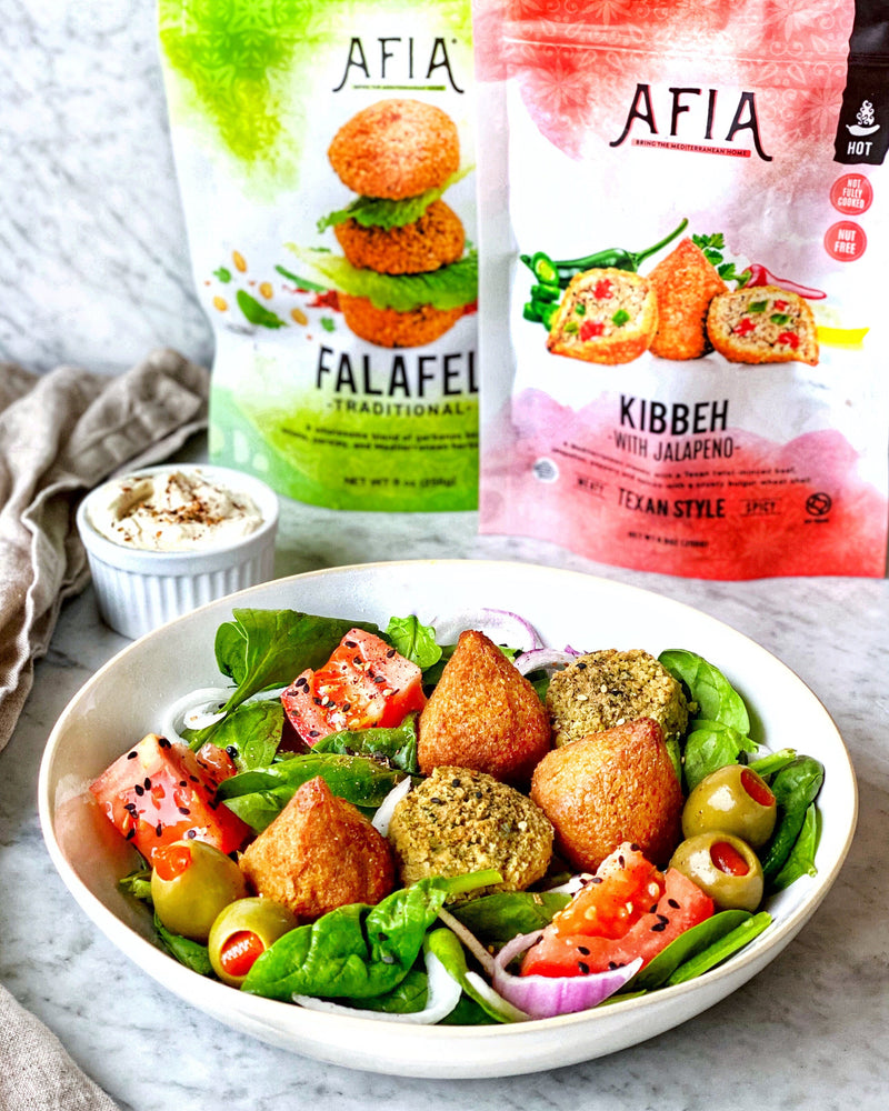 Spinach salad in a bowl topped with Afia Kibbeh and Falafel.