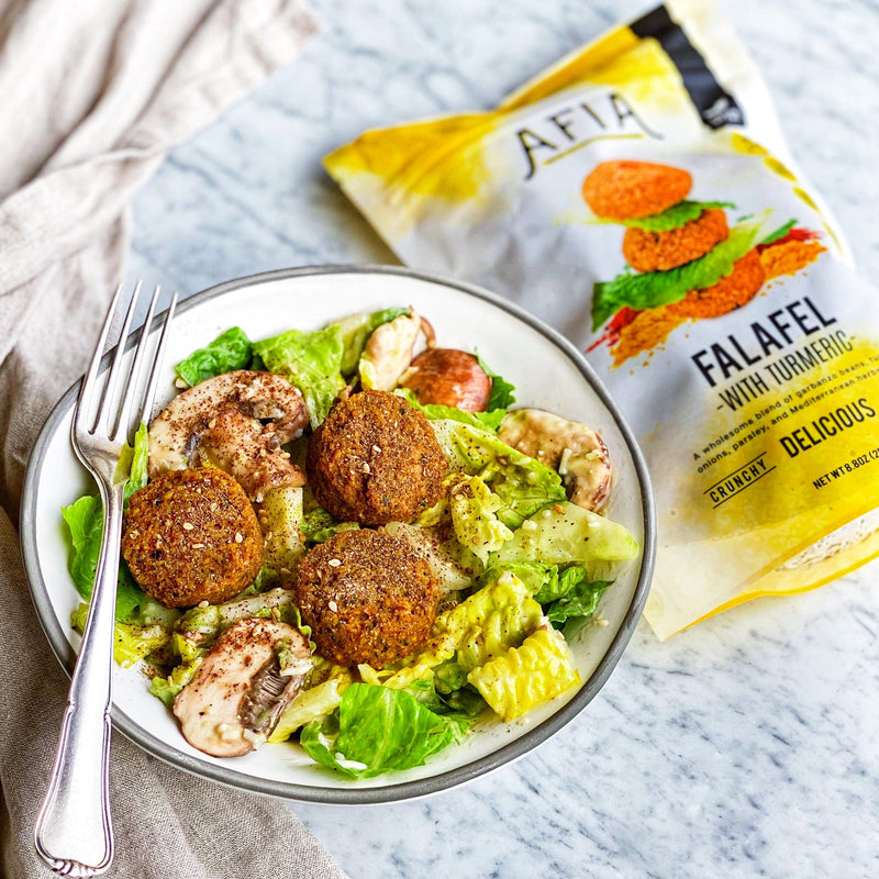 Caesar salad in a bowl topped with Afia Falafel. 