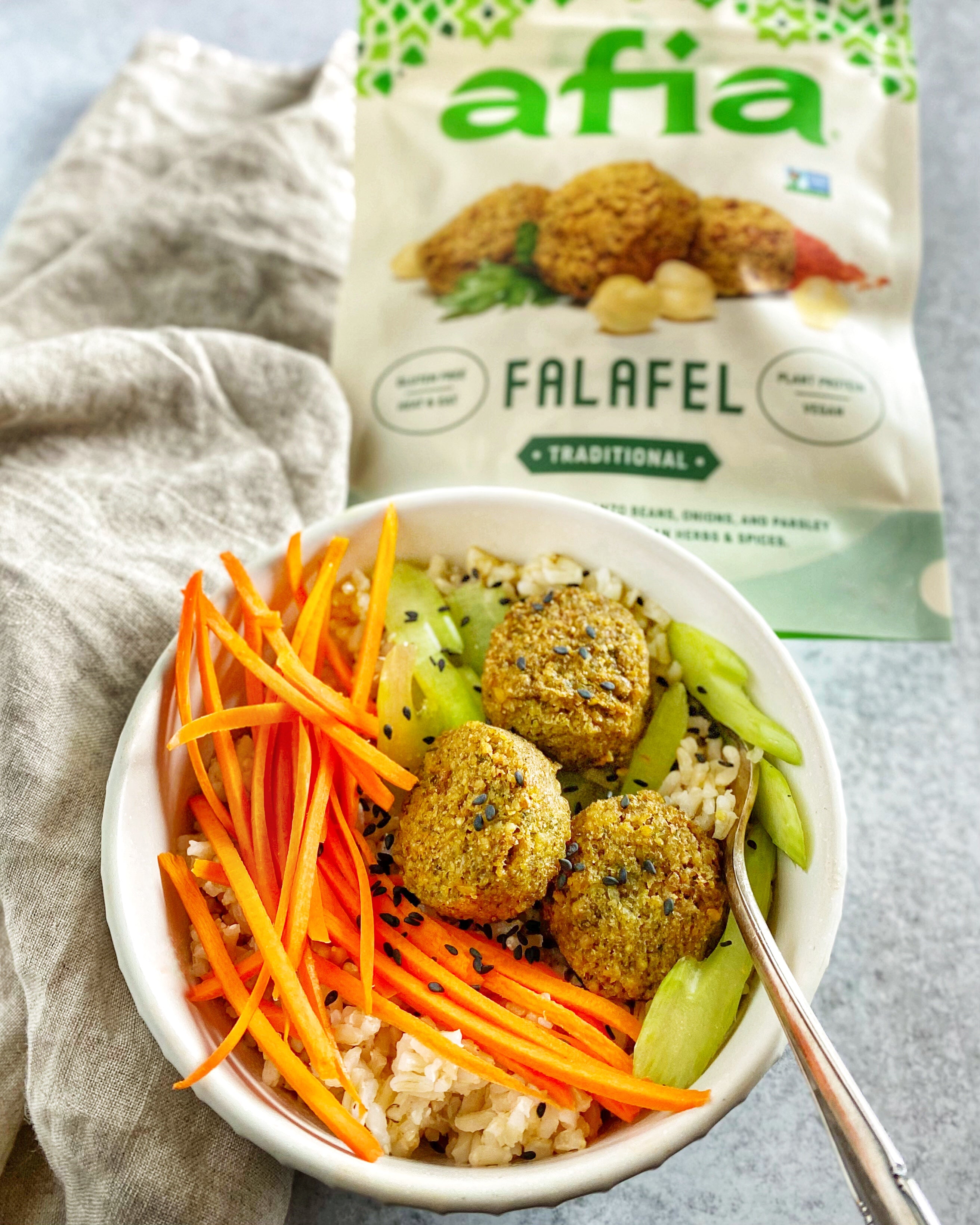 Healthy Traditional Falafel Bowl With Veggies and Black Sesame Seeds, next to a bag of Traditional Afia Falafel