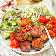 Afia Sun-Dried Tomato Falafel on a plate with other fresh vegetables, including tomato and avocado. 